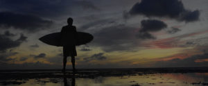 Silhouette of a surfer standing on the beach at sunset